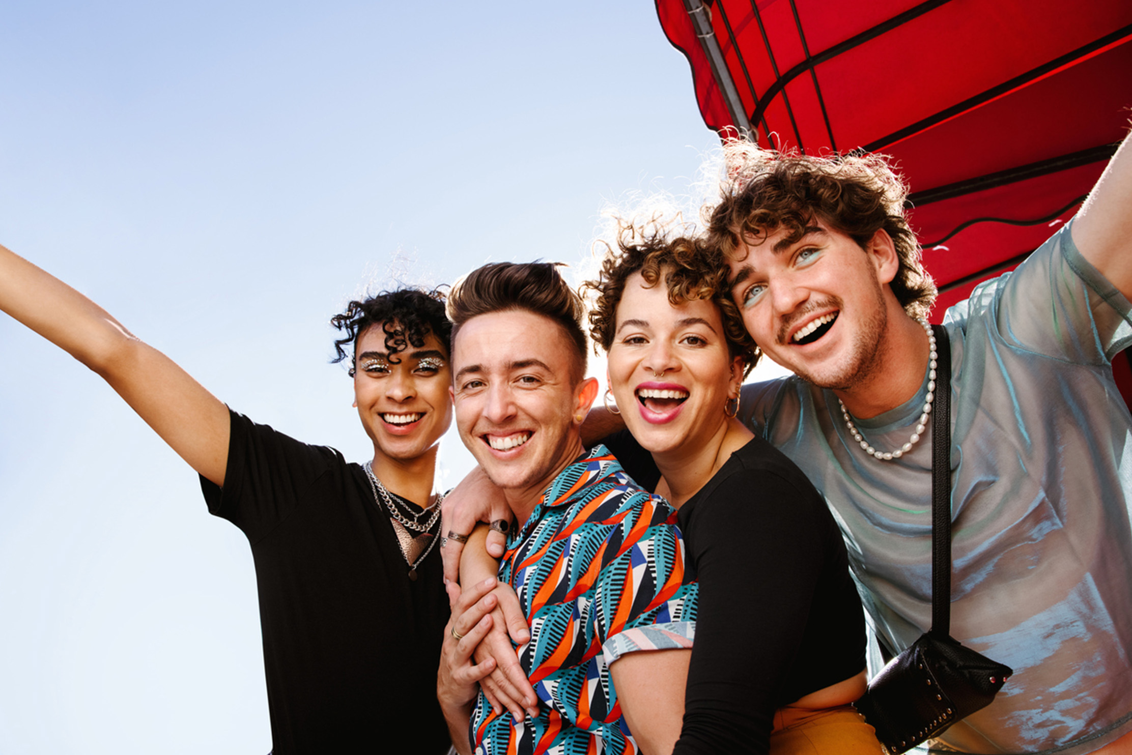 Four young queer people smiling while standing together and embracing each other. 
