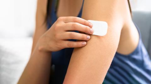 A lady applies a contraceptive patch to her arm