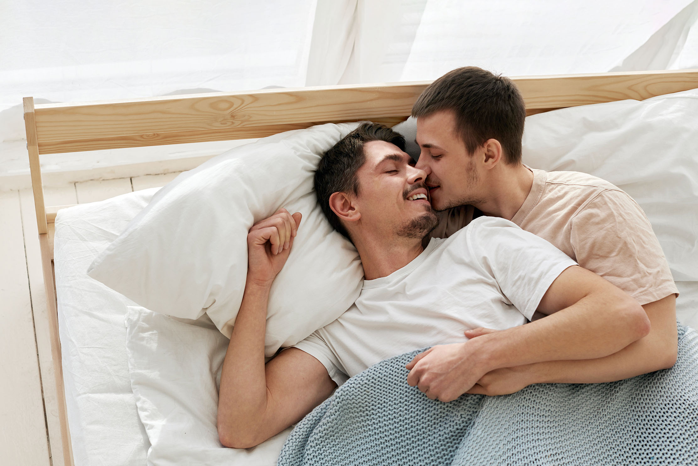A same sex couple kiss and cuddle in bed