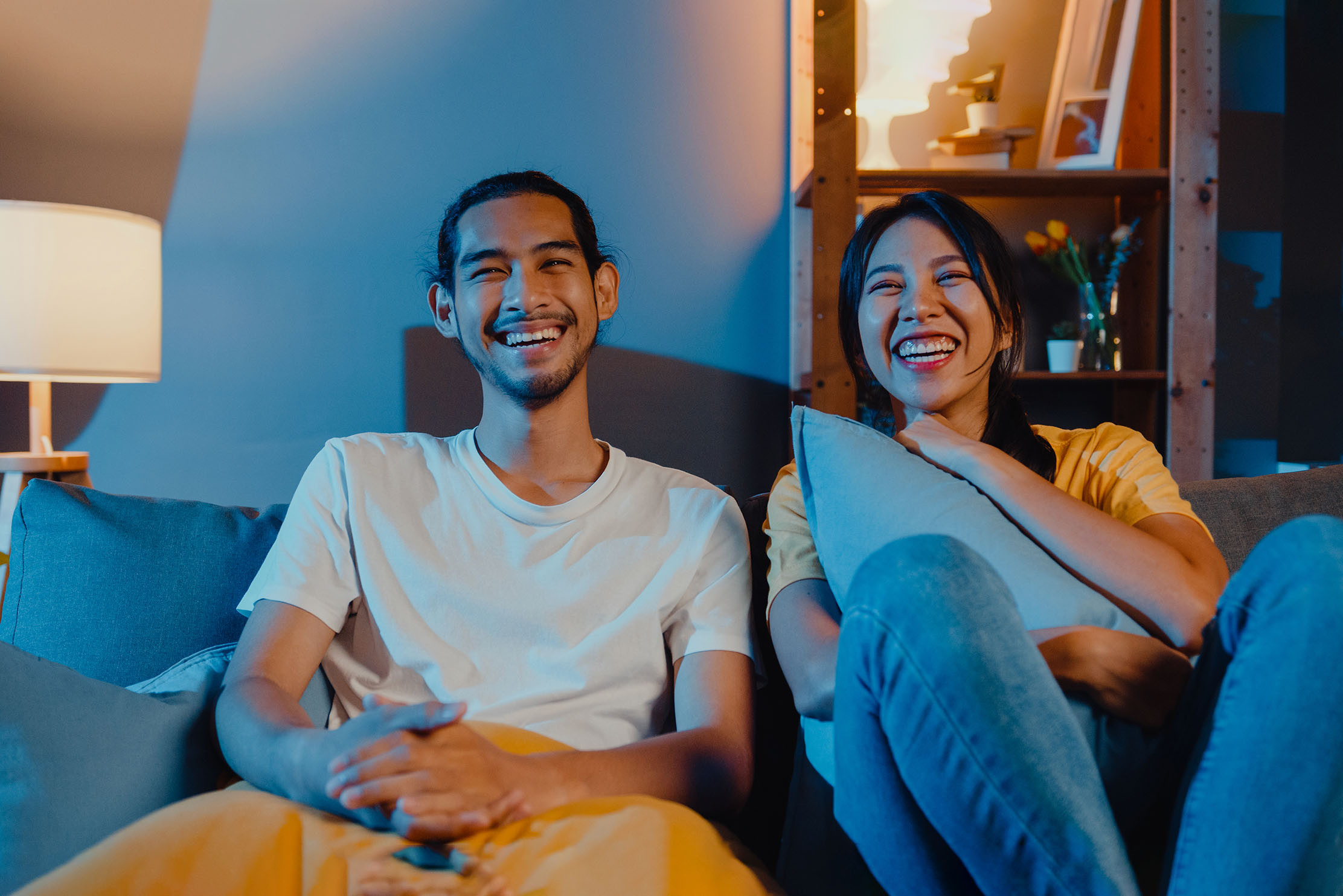 A young asian couple laugh while sat on the sofa