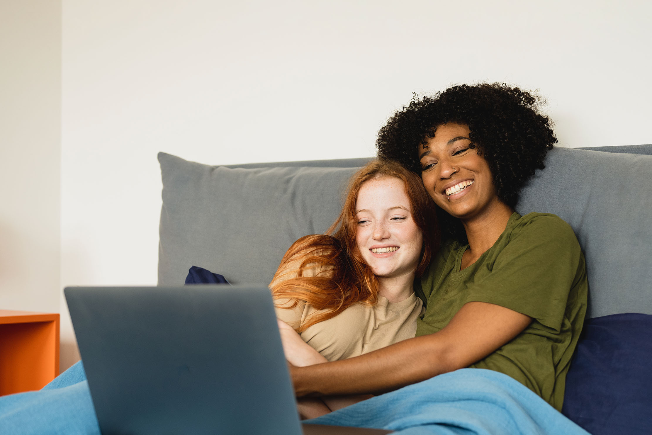 A mixed race couple cuddle in bed whilst looking at a laptop