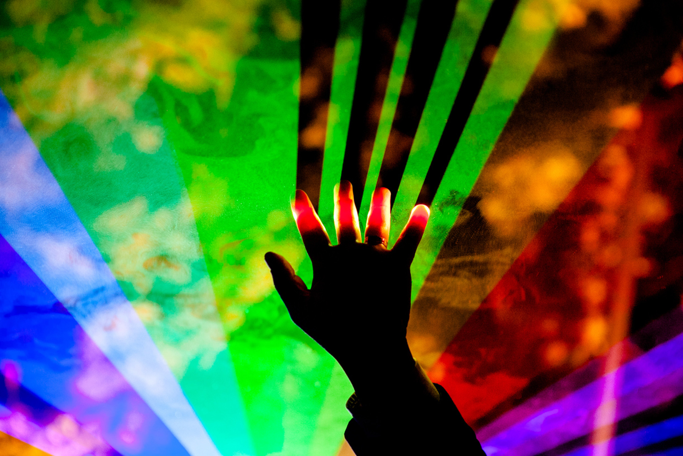 A hand raised in the air, penetrating rainbow lights