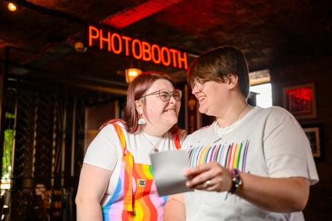 lesbian couple at a photobooth smiling at a photograph